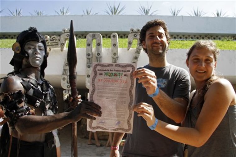 A man dressed as a Mayan warrior delivers a life certificate for one million dollars, to be paid in case the world comes to an end to an unidentified couple, as they pose for a photo at the Xcaret theme park in Playa del Carmen, Mexico, Saturday, Dec. 15, 2012.  Amid a worldwide frenzy of advertisers and new-agers preparing for a Maya apocalypse, one group is approaching Dec. 21 with calm and equanimity calm: the people whose ancestors supposedly made the prediction in the first place. Mexico's 800,000 Mayas are not the sinister, secretive, apocalypse-obsessed race they've been made out to be.  (AP Photo/Israel Leal)